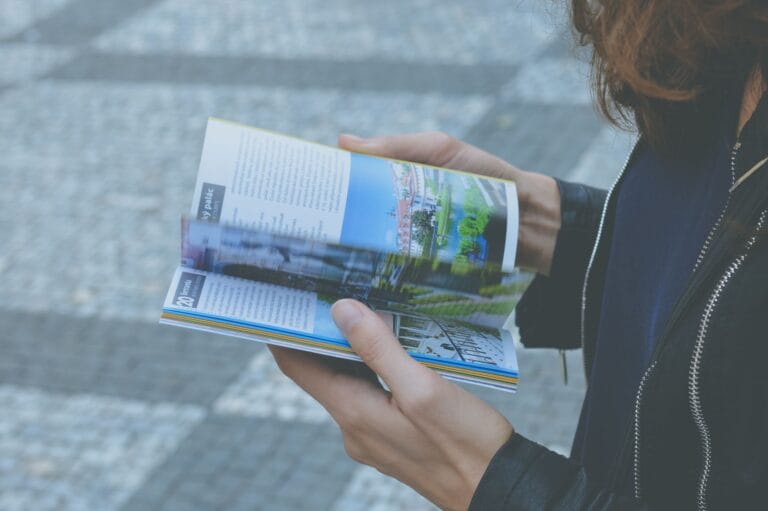 Osoba przeglądająca kolorowy katalog podróży na świeżym powietrzu